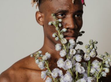 Man with acne holding flowers partly in front of his face.
