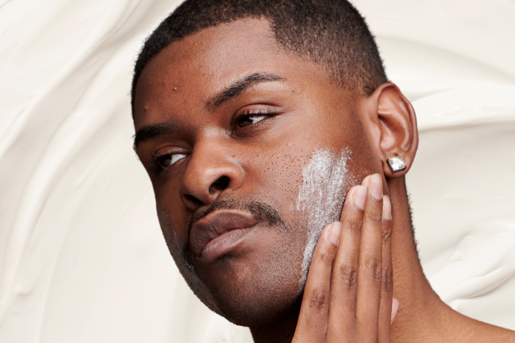 Man with mild acne practices face basting by applying thick white cream to face